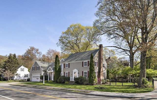 colonial house with a chimney, driveway, fence, an attached garage, and a front lawn