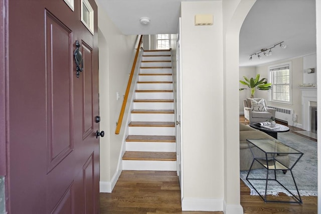 stairway with wood finished floors, radiator heating unit, a fireplace, arched walkways, and baseboards