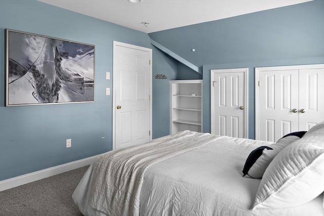 carpeted bedroom with vaulted ceiling, two closets, and baseboards