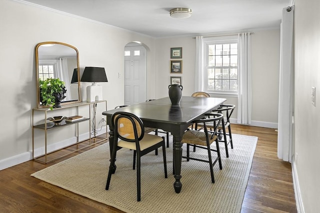 dining space featuring ornamental molding, arched walkways, baseboards, and wood finished floors
