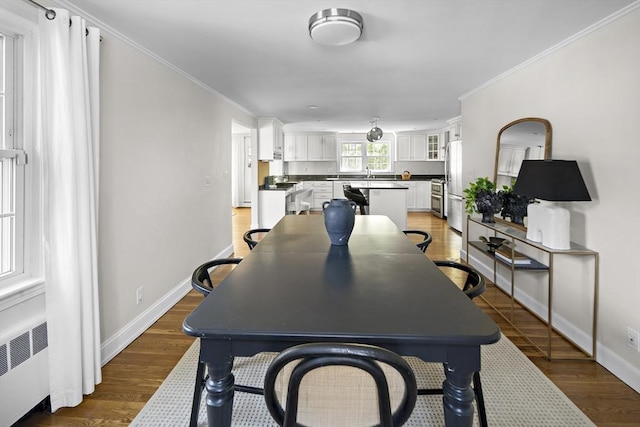 dining space featuring crown molding, light wood-style flooring, baseboards, and radiator heating unit