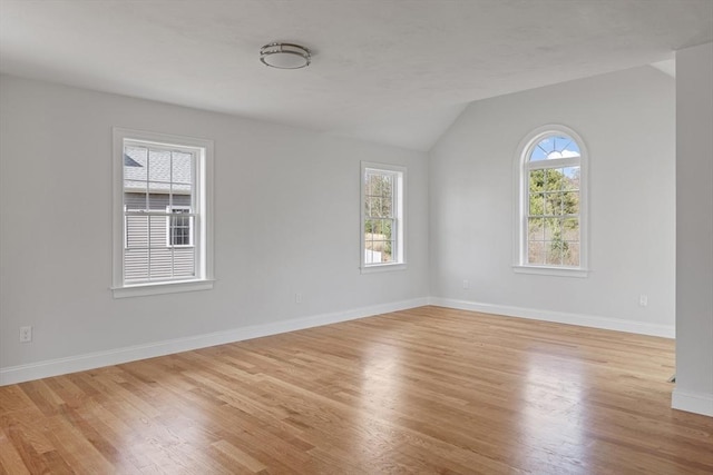 spare room with vaulted ceiling, light wood finished floors, and baseboards