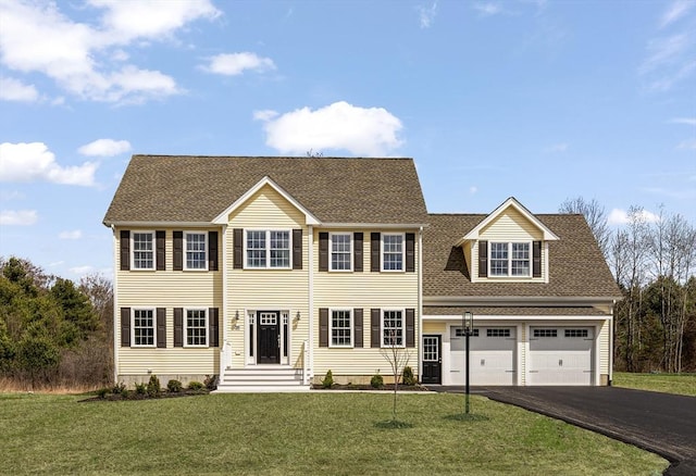 colonial house with an attached garage, driveway, a shingled roof, and a front yard