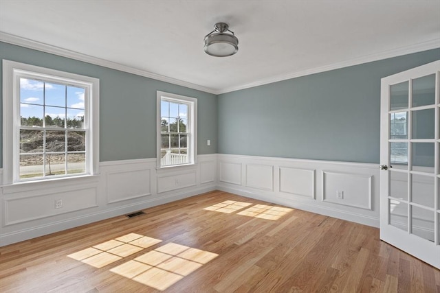 empty room featuring a wainscoted wall, visible vents, and ornamental molding