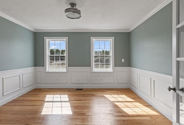 unfurnished room featuring light wood-style floors, a wealth of natural light, and a wainscoted wall