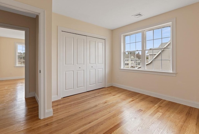 unfurnished bedroom featuring light wood-type flooring, baseboards, visible vents, and a closet