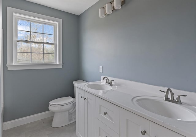 bathroom with baseboards, a sink, double vanity, and toilet