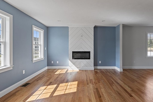 unfurnished living room with baseboards, a large fireplace, wood finished floors, and visible vents