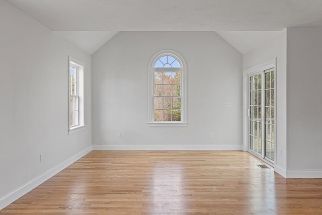 spare room featuring lofted ceiling, light wood finished floors, and baseboards
