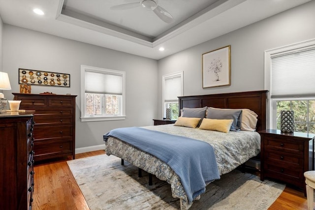 bedroom featuring light wood finished floors, recessed lighting, a raised ceiling, and baseboards