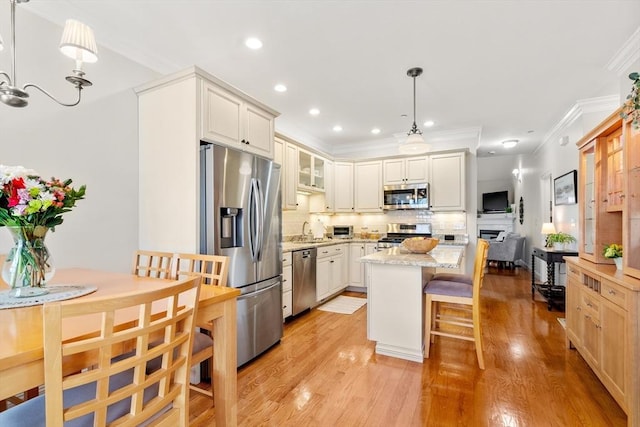 kitchen featuring light wood-type flooring, ornamental molding, a sink, tasteful backsplash, and appliances with stainless steel finishes