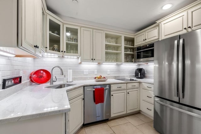 kitchen featuring a sink, backsplash, stainless steel appliances, light tile patterned floors, and glass insert cabinets