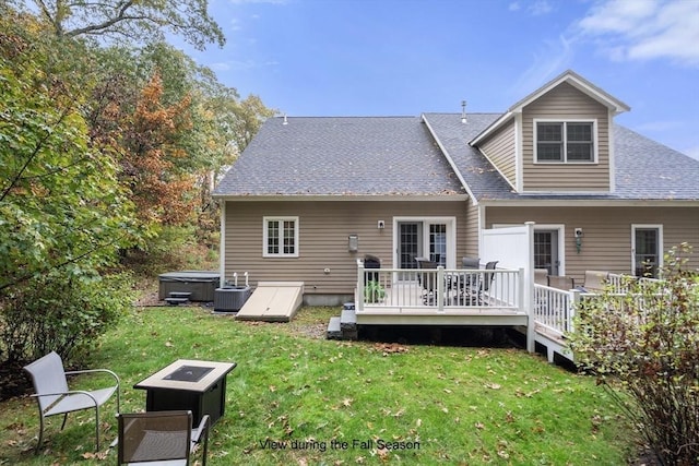 back of house featuring cooling unit, an outdoor fire pit, a wooden deck, a hot tub, and a lawn