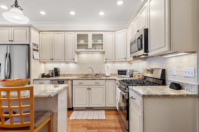 kitchen featuring light wood-type flooring, a sink, tasteful backsplash, stainless steel appliances, and hanging light fixtures