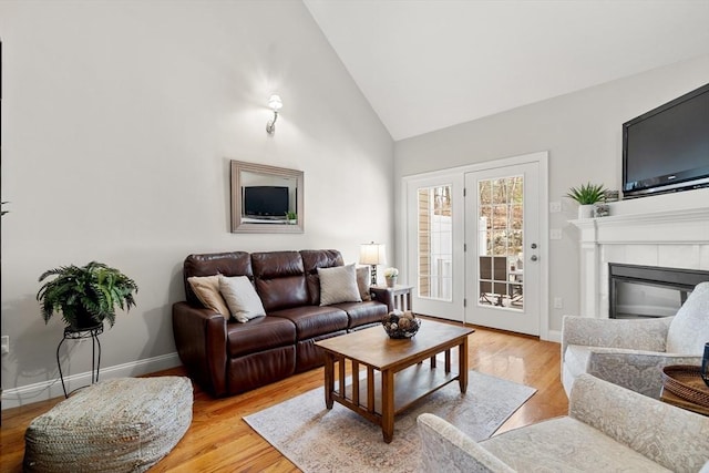 living area featuring a tiled fireplace, light wood-style flooring, high vaulted ceiling, and baseboards