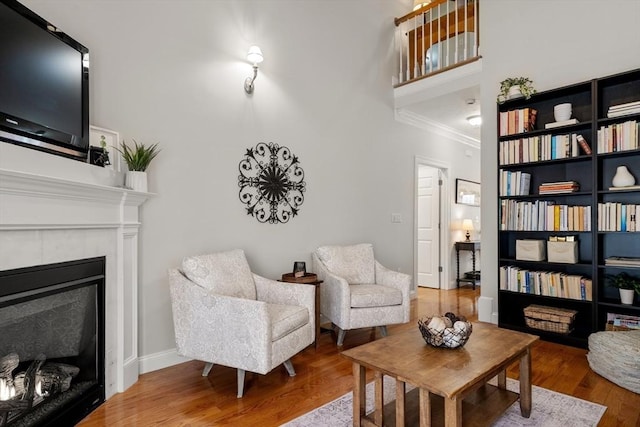 living room with a glass covered fireplace, baseboards, wood finished floors, and ornamental molding