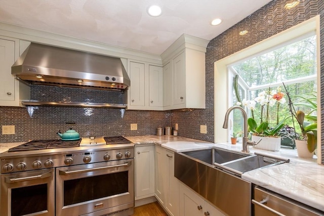 759 Main St, Boxford, MA 01921 - kitchen with stainless steel appliances, wall chimney range hood, light stone countertops, white cabinets, and recessed lighting