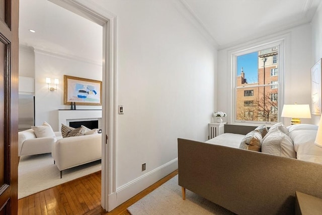 bedroom with ornamental molding, wood-type flooring, and a brick fireplace