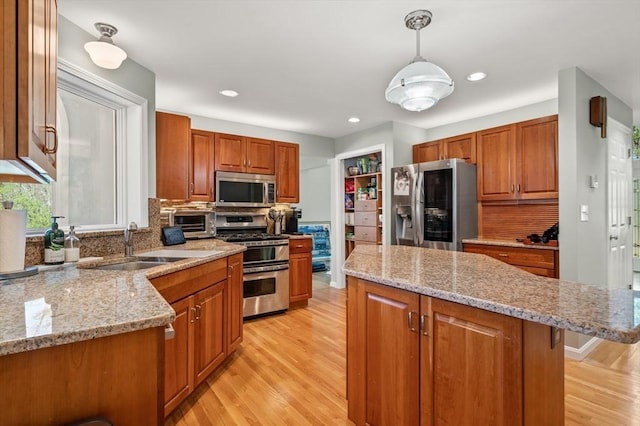 kitchen with a sink, light wood-style flooring, appliances with stainless steel finishes, and a kitchen island