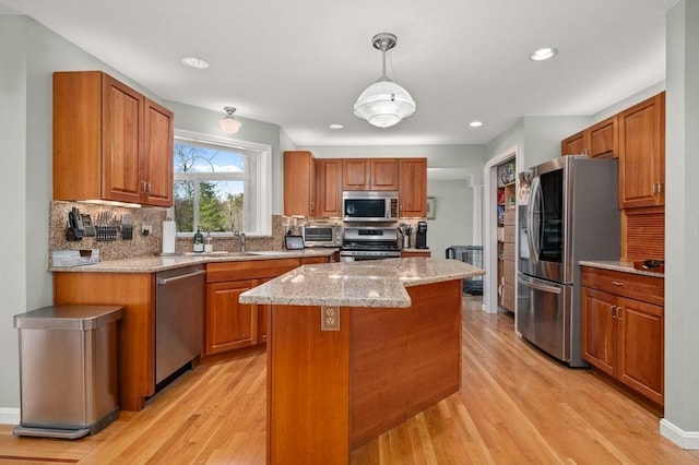 kitchen with brown cabinetry, light wood-style floors, a center island, tasteful backsplash, and appliances with stainless steel finishes