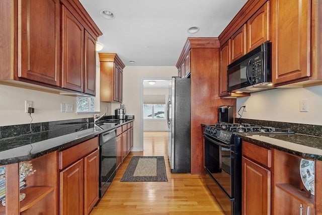 kitchen with dark stone countertops, sink, light hardwood / wood-style flooring, and black appliances