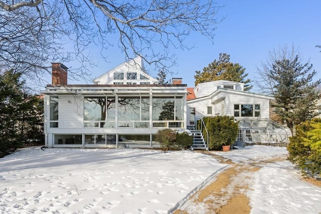 snow covered back of property featuring a sunroom