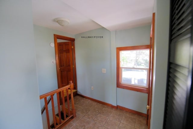 corridor with baseboards, light tile patterned floors, and an upstairs landing