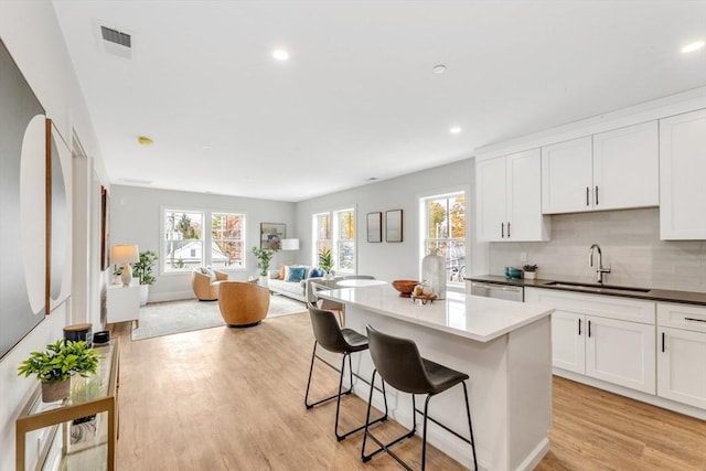 kitchen featuring light wood-style flooring, a kitchen island, open floor plan, a kitchen bar, and a sink