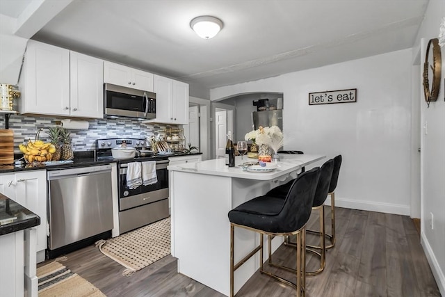631 Chestnut St, Athol, MA 01331 - kitchen featuring appliances with stainless steel finishes, white cabinetry, decorative backsplash, dark wood-style flooring, and a kitchen breakfast bar
