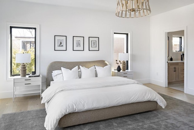 bedroom with baseboards, light wood-type flooring, and an inviting chandelier