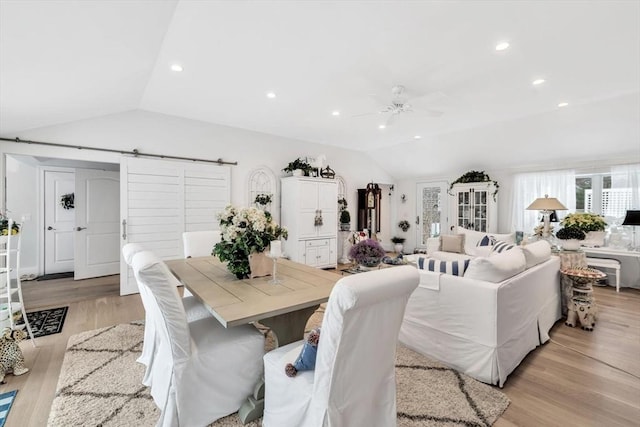 dining room featuring light hardwood / wood-style flooring, vaulted ceiling, and a barn door