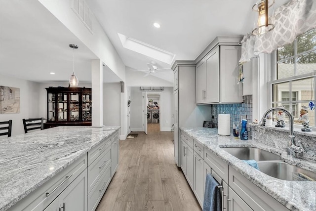 kitchen featuring gray cabinets, light stone countertops, sink, and backsplash