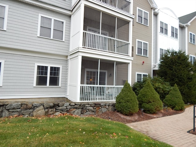 rear view of property featuring a balcony, a yard, and a sunroom