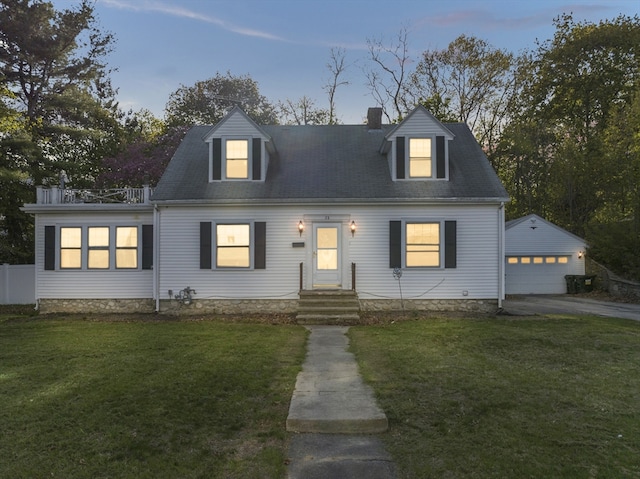 cape cod home with a chimney, aphalt driveway, a front lawn, an outbuilding, and a detached garage