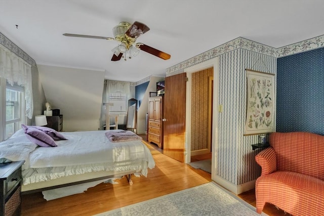 bedroom with a ceiling fan, wallpapered walls, and wood finished floors