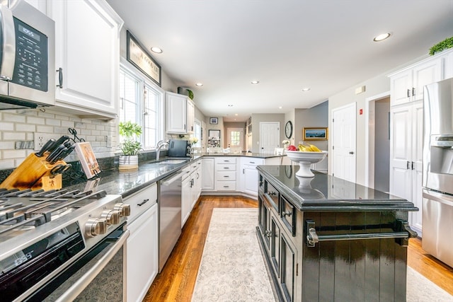 kitchen featuring appliances with stainless steel finishes, light wood-type flooring, a kitchen island, kitchen peninsula, and white cabinets