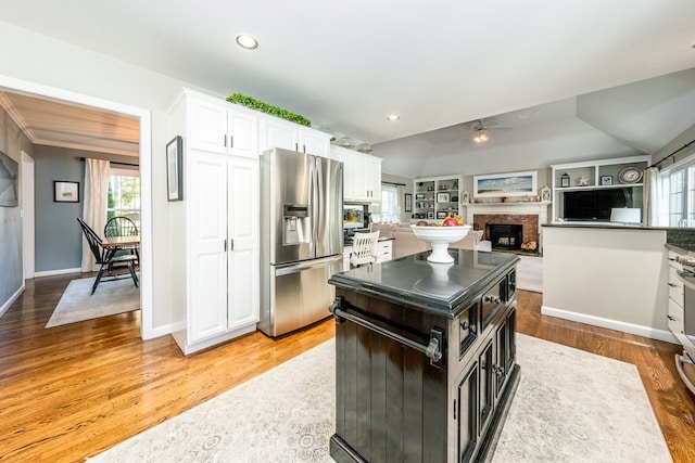 kitchen with stainless steel fridge with ice dispenser, white cabinetry, a fireplace, light hardwood / wood-style floors, and ceiling fan