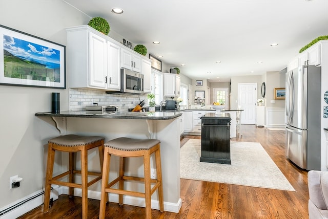 kitchen featuring kitchen peninsula, stainless steel appliances, wood-type flooring, a baseboard radiator, and white cabinets