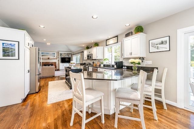 kitchen with appliances with stainless steel finishes, light wood-type flooring, backsplash, kitchen peninsula, and white cabinets