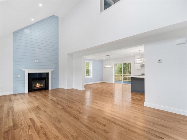 316 Old Westport Rd, Dartmouth, MA 02747 - unfurnished living room featuring high vaulted ceiling, light wood-type flooring, a warm lit fireplace, baseboards, and a chandelier