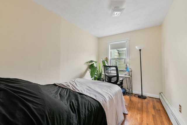 bedroom with a baseboard heating unit, light wood finished floors, and baseboards