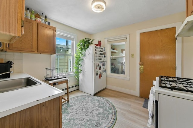 kitchen with white appliances, baseboard heating, light wood-style floors, tasteful backsplash, and light countertops