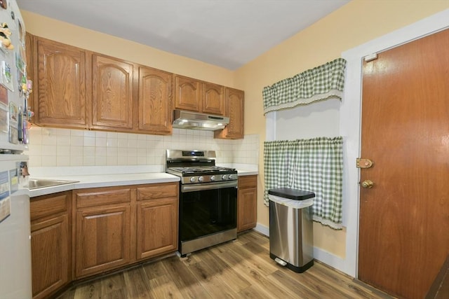 kitchen featuring stainless steel range with gas cooktop, under cabinet range hood, dark wood finished floors, decorative backsplash, and light countertops
