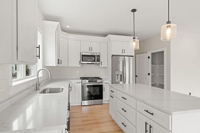kitchen featuring white cabinets, hanging light fixtures, appliances with stainless steel finishes, a sink, and a center island