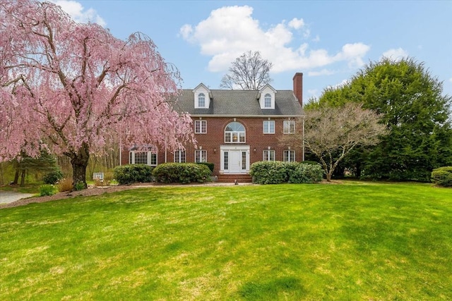 exterior space with brick siding, a front yard, and a chimney