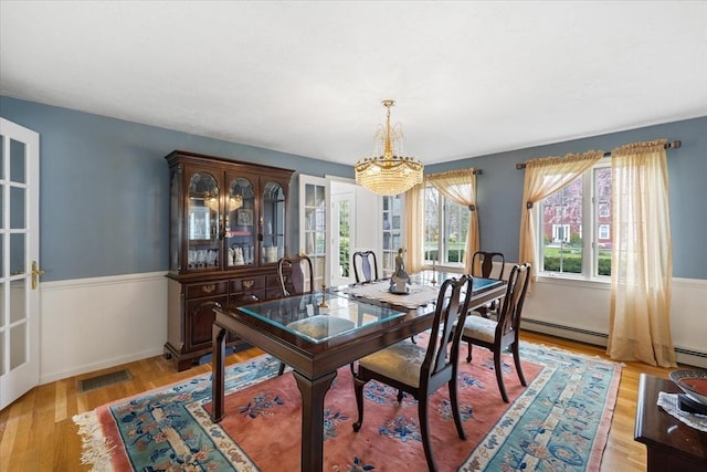dining room with an inviting chandelier, a baseboard heating unit, light wood finished floors, and visible vents