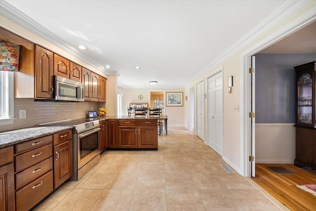 kitchen featuring visible vents, ornamental molding, a peninsula, baseboards, and stainless steel appliances