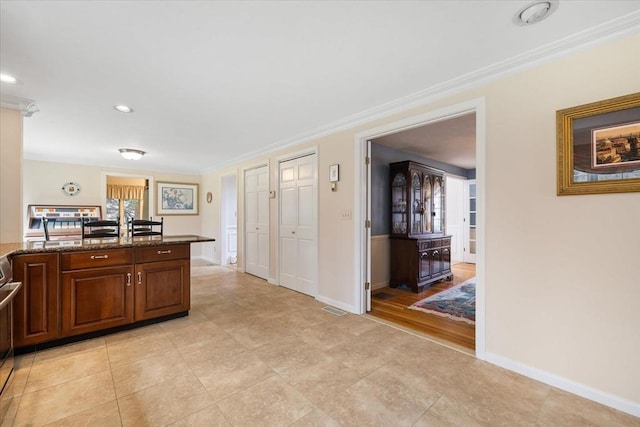 kitchen with crown molding, baseboards, visible vents, and dark stone counters