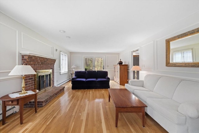 living area with a decorative wall, a baseboard heating unit, light wood-style flooring, and a brick fireplace