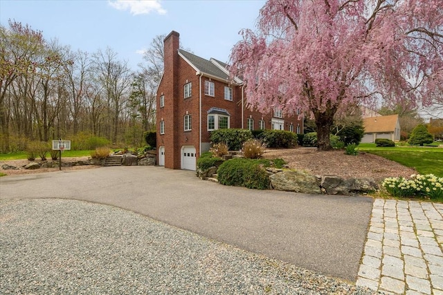 view of side of property featuring an attached garage, a chimney, brick siding, and aphalt driveway